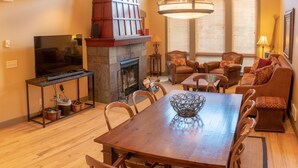 A cozy living room with a fireplace, a dining table, and comfortable seating. - 7401- Three Bedroom + Loft + Den Deluxe Crossings Townhomes 3 Condo by RedAwning (Solitude)