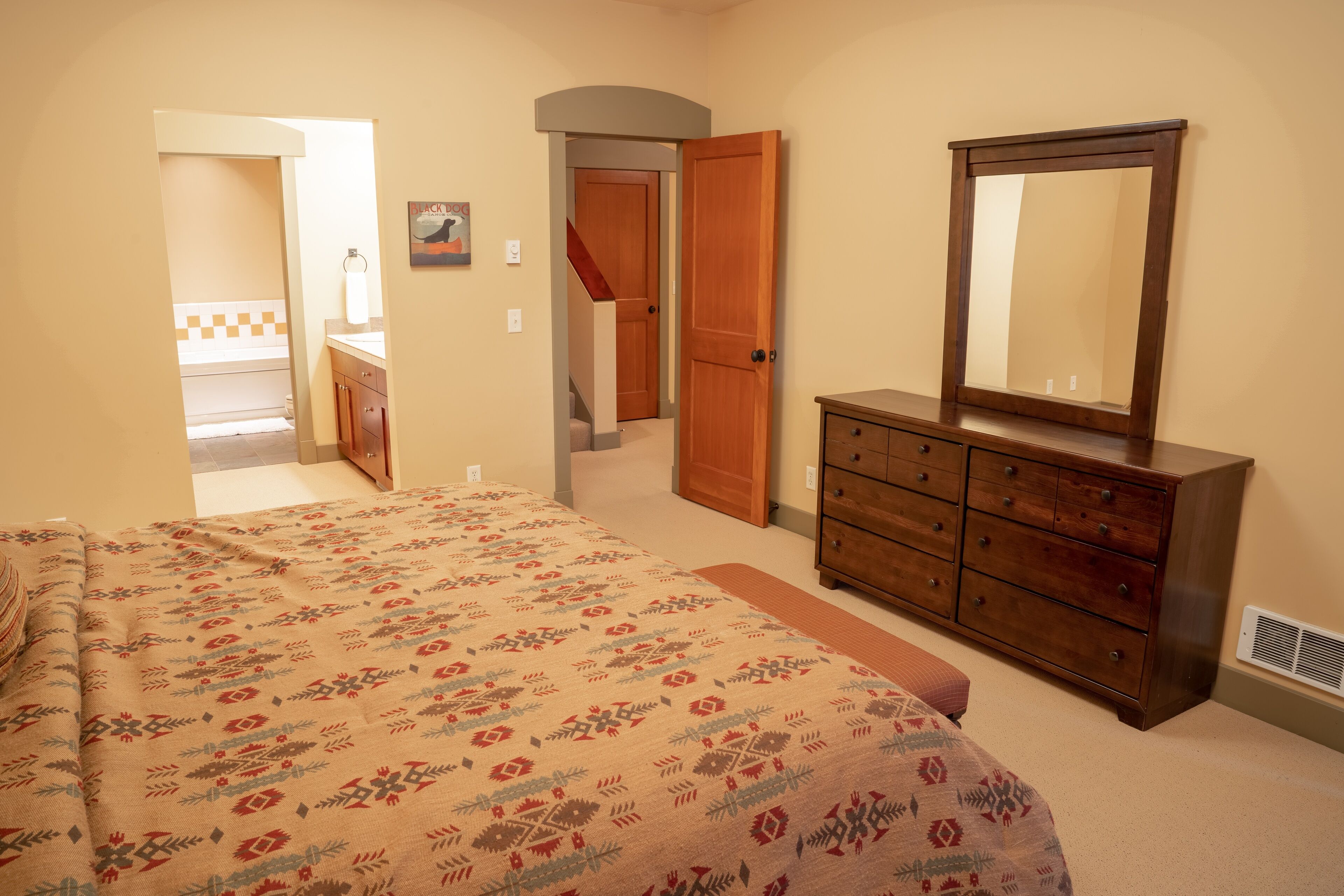 Une chambre à coucher comprenant un lit, une commode et une porte donnant sur une autre pièce.