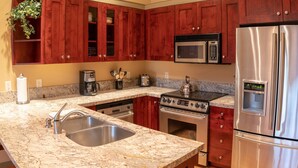 A kitchen with wooden cabinets, a stainless steel refrigerator, a microwave, a stove, and a sink. - 7401- Three Bedroom + Loft + Den Deluxe Crossings Townhomes 3 Condo by RedAwning (Solitude)