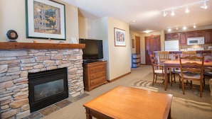 A living room with a stone fireplace, a television, and a dining area with wooden furniture. - 3313 - One Bedroom + Den Standard Powderhorn Lodge 1 Condo by RedAwning (Salt Lake City)