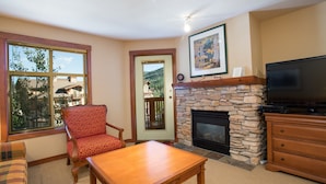 A living room with a stone fireplace, a television, a wooden table, and a red patterned chair. - 3313 - One Bedroom + Den Standard Powderhorn Lodge 1 Condo by RedAwning (Salt Lake City)