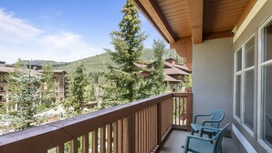 A balcony with a wooden railing, two green plastic chairs, and a view of a mountainous area with buildings in the background. - 3313 - One Bedroom + Den Standard Powderhorn Lodge 1 Condo by RedAwning (Salt Lake City)