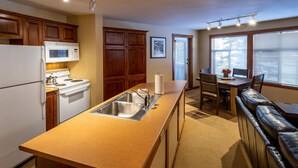 Cocina compacta con isla central, armarios de madera, microondas integrado y comedor con banco y mesa.