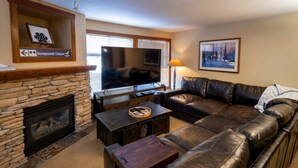Una sala de estar con chimenea de piedra, sofá de cuero y televisor de pantalla plana.