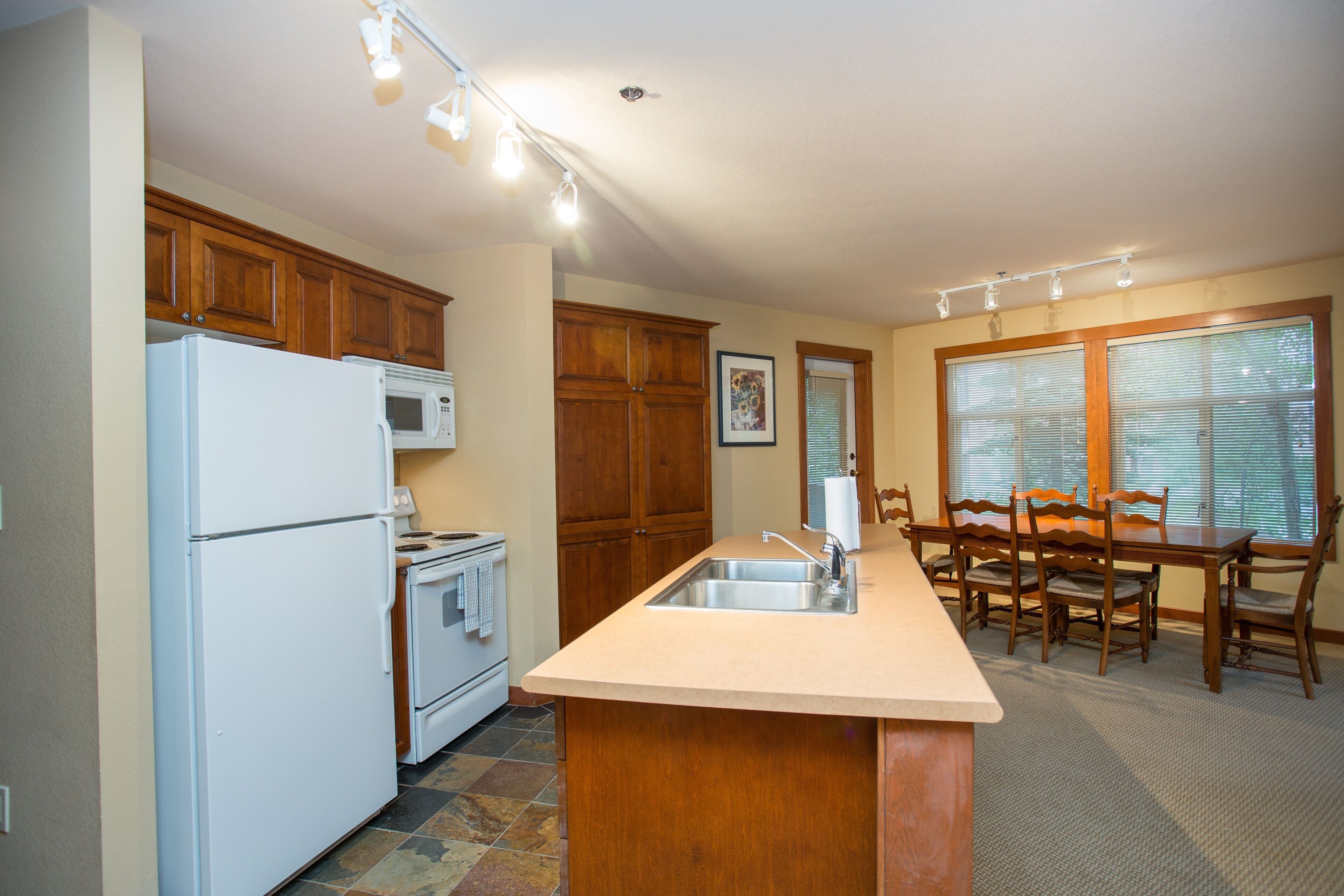 A kitchen with wooden cabinets, a white refrigerator, a microwave, and a sink. There is a dining area with a table and chairs.