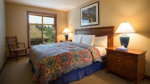 A bedroom with a large bed, two bedside lamps, a wooden nightstand, a chair, and a window with a view of trees. - 3219 - Three Bedroom Standard Powderhorn Lodge 3 Condo by RedAwning (Salt Lake City)