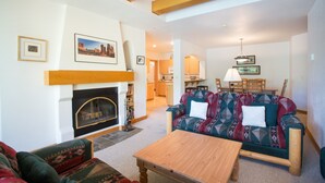 Una sala de estar con chimenea, un sofá, una mesa de centro y una zona de comedor con sillas y una lámpara.