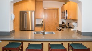 Una cocina con refrigerador de acero inoxidable, gabinetes de madera, un lavamanos y taburetes de bar.