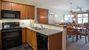 Una cocina con armarios de madera, microondas, estufa y lavavajillas. Hay un comedor con una mesa y sillas.