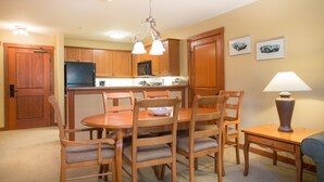 Cocina compacta con armarios de madera, un refrigerador y un comedor con mesa y sillas.