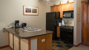 A kitchen with a granite countertop, stainless steel sink, black refrigerator, stove, microwave, and wooden cabinets.
