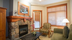 A living room with a stone fireplace, a framed picture above it, a green armchair, a sofa, and a window with blinds.