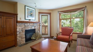 A living room with a stone fireplace, wooden furniture, and a large window with curtains. - 3406 - One Bedroom + Den Standard Powderhorn Lodge 1 Condo by RedAwning (Salt Lake City)