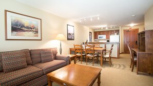 A living room with a sofa, a wooden coffee table, and a dining area with a table and chairs. - 3406 - One Bedroom + Den Standard Powderhorn Lodge 1 Condo by RedAwning (Salt Lake City)