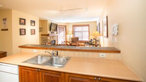 A kitchen with a built-in sink, wooden cabinets, a stone backsplash, and a television mounted above the fireplace. - 3216 - One Bedroom + Den Standard Powderhorn Lodge 1 Condo by RedAwning (Salt Lake City)