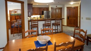 Un'area pranzo con tavolo in legno, sedie, un cesto e una cucina sullo sfondo.