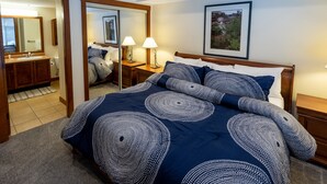 Una camera da letto con un letto grande, una testiera in legno, due comodini con lampade, uno specchio, un quadro appeso alla parete e un bagno visibile attraverso una porta aperta.