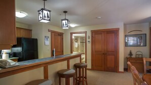 A kitchen with wooden cabinets, a black refrigerator, a bar area with stools, and a hanging light fixture. - 2202 - Two Bedroom Standard Eagle Springs East 2 Condo by RedAwning (Solitude)