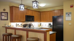 A kitchen with wooden cabinets, a black refrigerator, a microwave, and a bar stool. - 2202 - Two Bedroom Standard Eagle Springs East 2 Condo by RedAwning (Solitude)