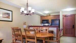 A dining area with a wooden table and chairs, a chandelier, and wooden cabinets. - 2203 - One Bedroom + Den Standard Eagle Springs East 1 Condo by RedAwning (Solitude)