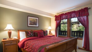 A neatly made bed with a patterned bedspread, two bedside tables with lamps, a framed picture on the wall, and a window with curtains. - 2203 - One Bedroom + Den Standard Eagle Springs East 1 Condo by RedAwning (Solitude)