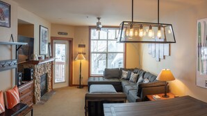 A cozy living room with a stone fireplace, a large window with blinds, a modern ceiling fan, and a comfortable sofa set. - 3505 - One Bedroom + Den Standard Powderhorn Lodge 1 Condo by RedAwning (Salt Lake City)