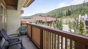A balcony with two Adirondack chairs, a wooden railing, and a view of a mountain landscape with buildings. - 3505 - One Bedroom + Den Standard Powderhorn Lodge 1 Condo by RedAwning (Salt Lake City)
