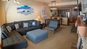 A modern living room with a sectional sofa, ottoman, and a dining area with a bar. - 3505 - One Bedroom + Den Standard Powderhorn Lodge 1 Condo by RedAwning (Salt Lake City)