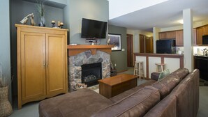 A living room with a stone fireplace, wooden cabinets, a television, and a brown leather sofa. - 2310 - Two Bedroom Standard Eagle Springs East 2 Condo by RedAwning (Solitude)