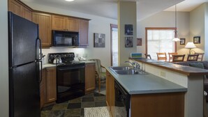 A kitchen with wooden cabinets, a black refrigerator, a microwave, an oven, a dishwasher, and a bar area with chairs. - 2310 - Two Bedroom Standard Eagle Springs East 2 Condo by RedAwning (Solitude)