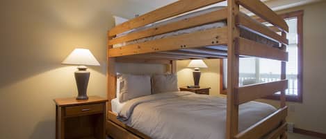 Una cama litera con estructura de madera, dos mesitas de noche con lámparas y una ventana con persianas.