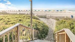 A wooden staircase leading to a beach area with a sandy path and a wooden fence.