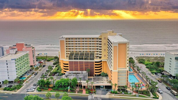A hotel with a pool, surrounded by greenery and a view of the ocean.