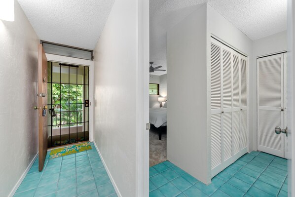 A hallway with a tiled floor, a door with a metal gate, and a room with a bed and a ceiling fan.