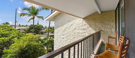 A balcony with a stone wall, wooden chairs, and a view of greenery and buildings.