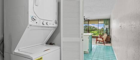 A laundry room with a white washer and dryer, a tiled floor, and a view of a balcony with a chair and a table.