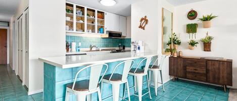 Una cocina moderna con una isla central, taburetes de bar, un microondas y un suelo de azulejos azul turquesa.