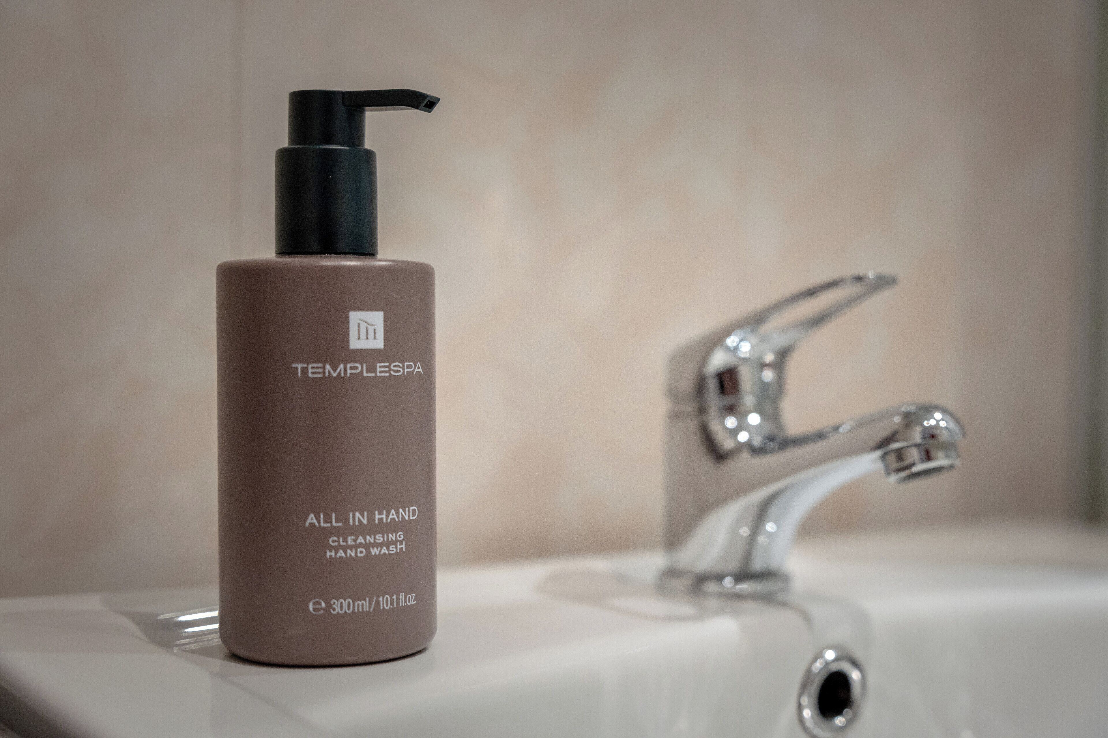 ”TEMPLESPA”-merkkinen käsisaippuan pullo on sijoitettu kylpyhuoneen pesualtaan viereen, ja altaassa on moderni hana.