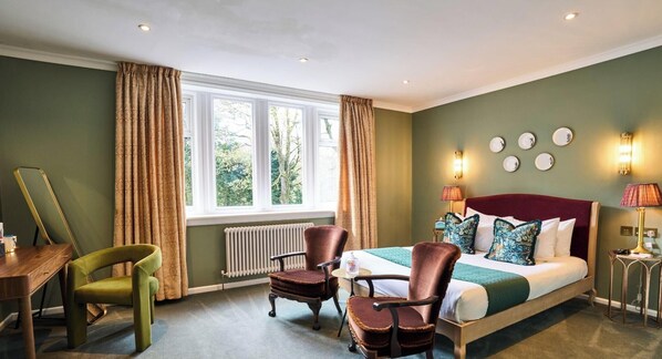 A hotel room with a bed, two chairs, a table, a window with curtains, a radiator, and wall-mounted lights. - Springbank Manor (Darwen)
