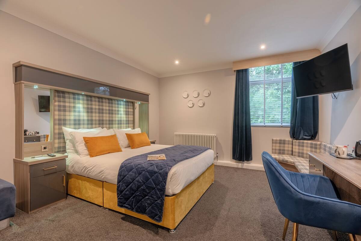 A modern hotel room with a bed, bedside table, chair, desk, and a TV.