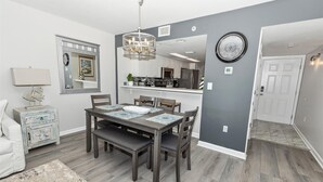 A dining area with a table set for four, a chandelier, and a kitchen in the background.