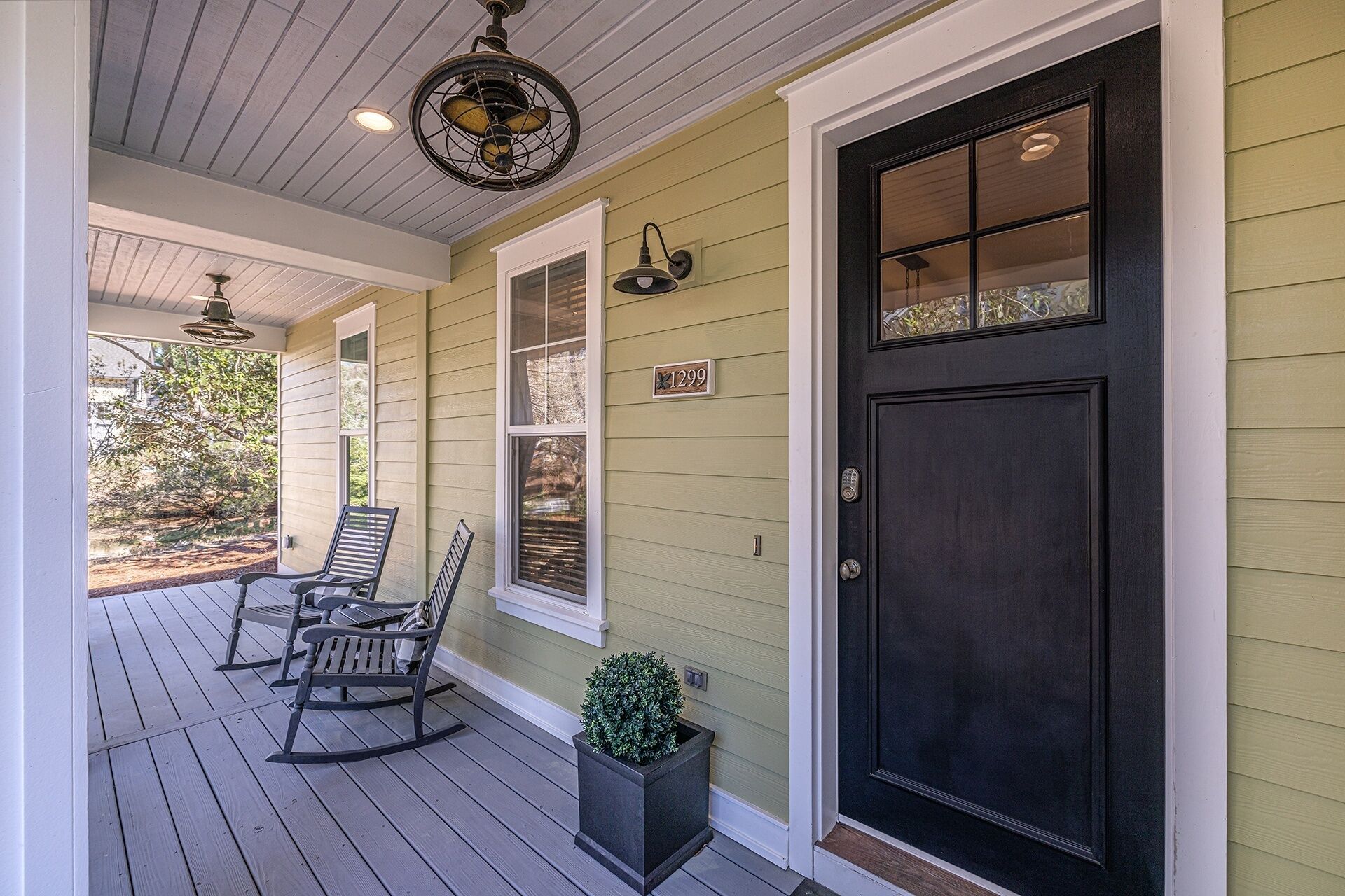 A porch with two rocking chairs, a potted plant, and a black door with a window.