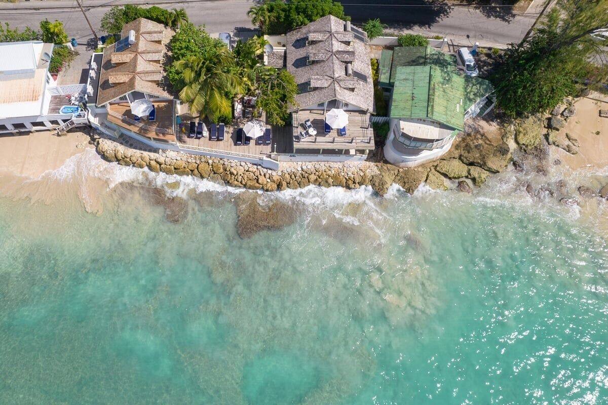 An aerial view of a coastal property with a beach, a pool, and a structure with a sloped roof.