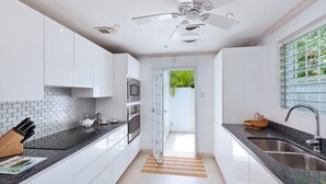 A modern kitchen with white cabinets, a black countertop, stainless steel appliances, and a view through an open door. - Easy Reach by Blue Sky Luxury (Mullins)