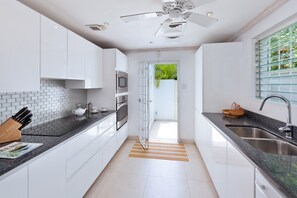 A modern kitchen with white cabinets, a black countertop, stainless steel appliances, and a view through an open door.
