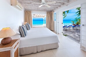 A bedroom with a bed, a nightstand, a lamp, and a view of the ocean through a door.