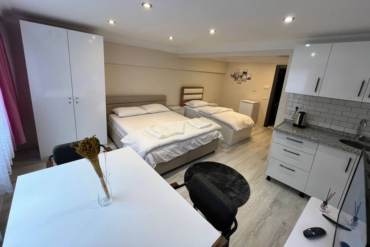 A hotel room with two beds, a desk, a chair, a small kitchenette, and a wardrobe.