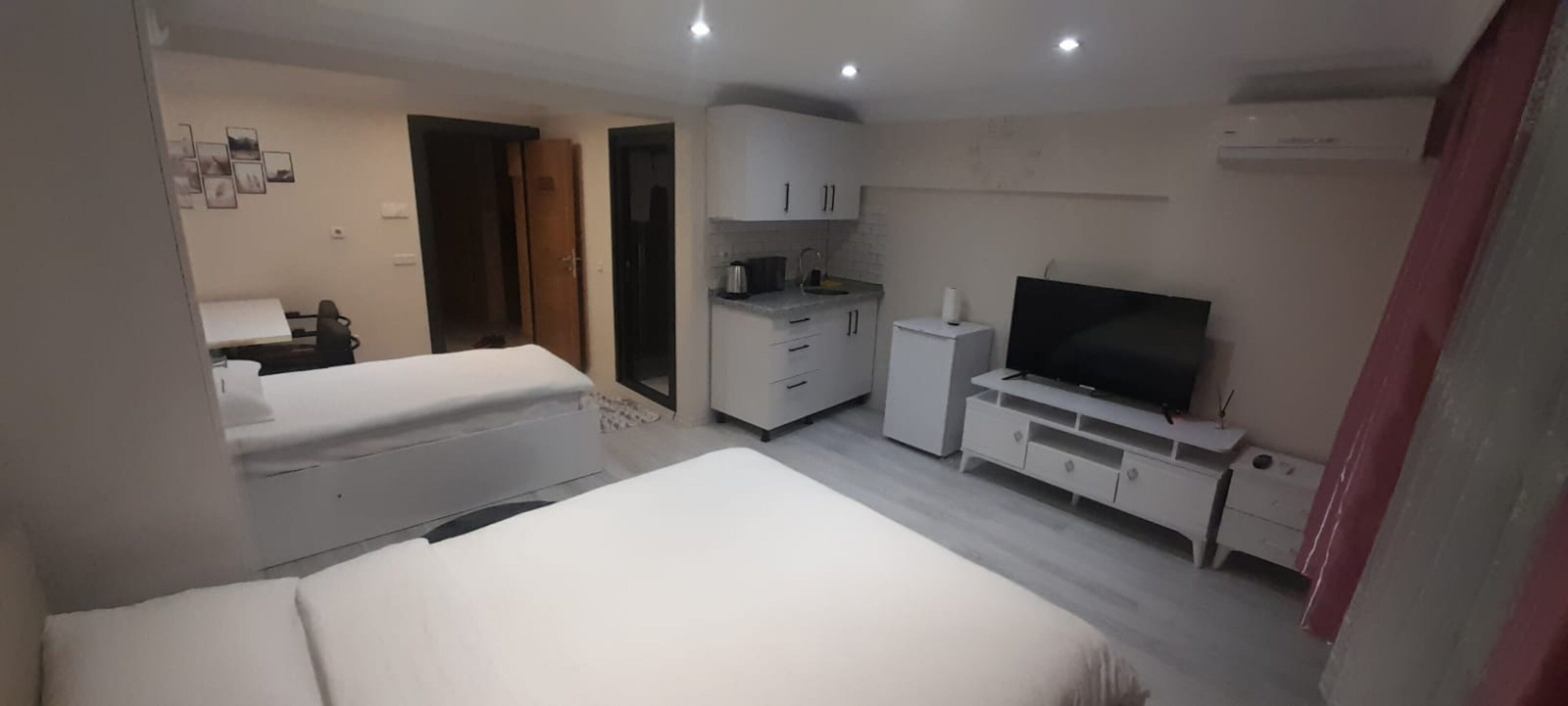 A hotel room with two beds, a TV, a kitchenette, and a bathroom.