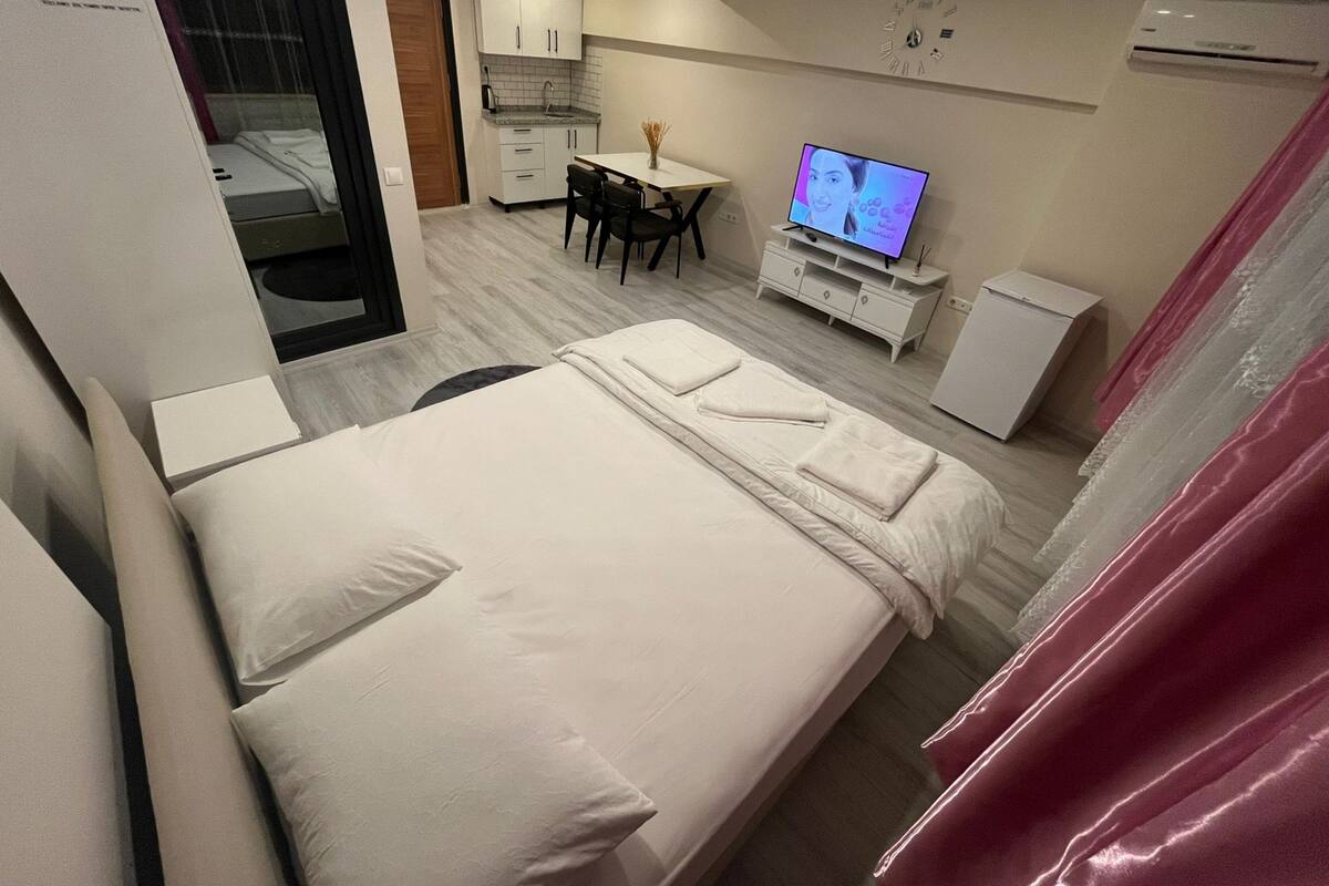 A hotel room with a bed, a desk, a TV, and a small kitchenette.