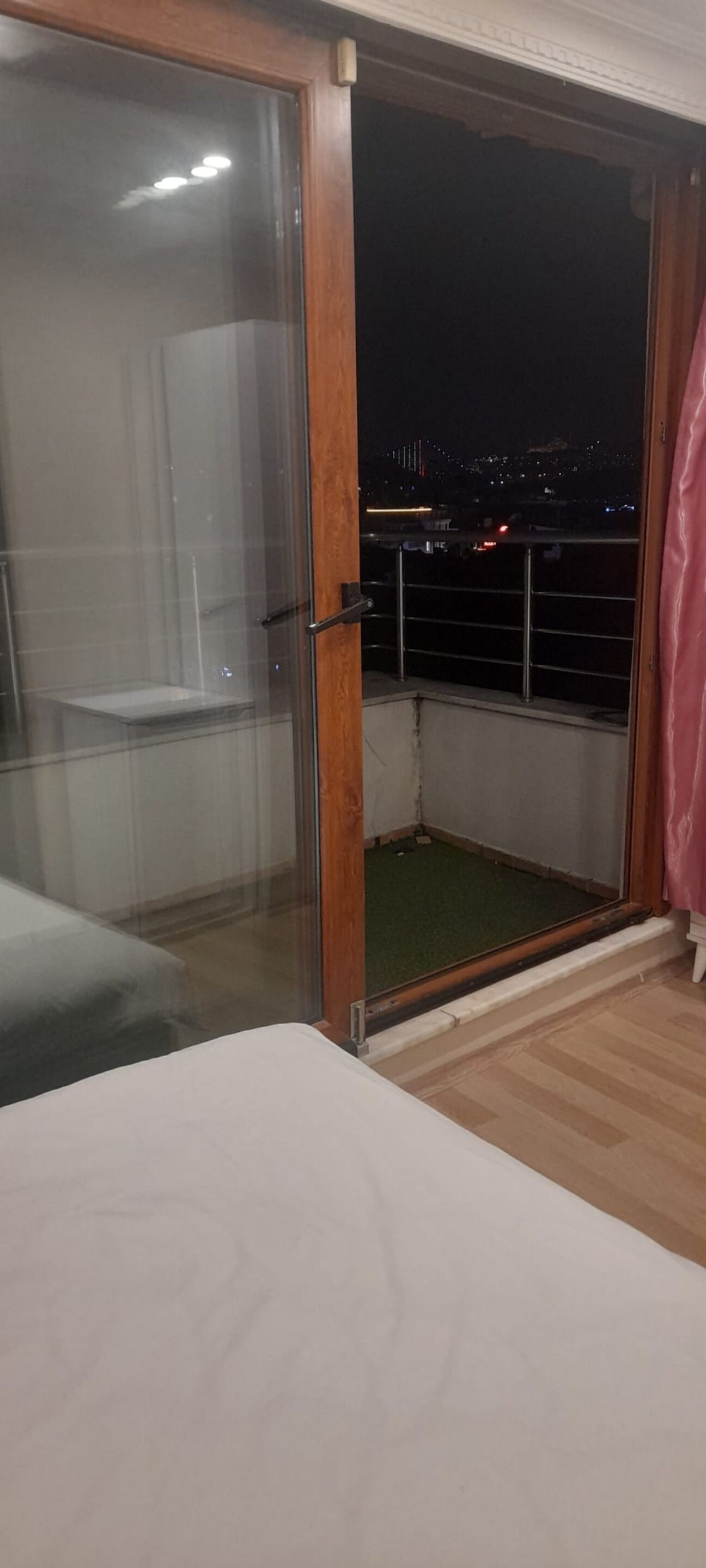 A room with a sliding glass door leading to a balcony. The balcony has a metal railing and a view of the city at night.